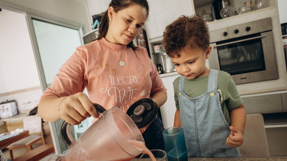 A mother pours a smoothie for her son in a home kitchen, showcasing family bonding.